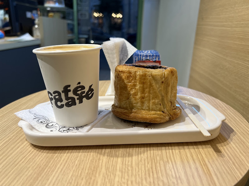 Vaso de Café Café con su logo en negro, junto a una factura sobre una bandeja, en una mesa de madera clara.